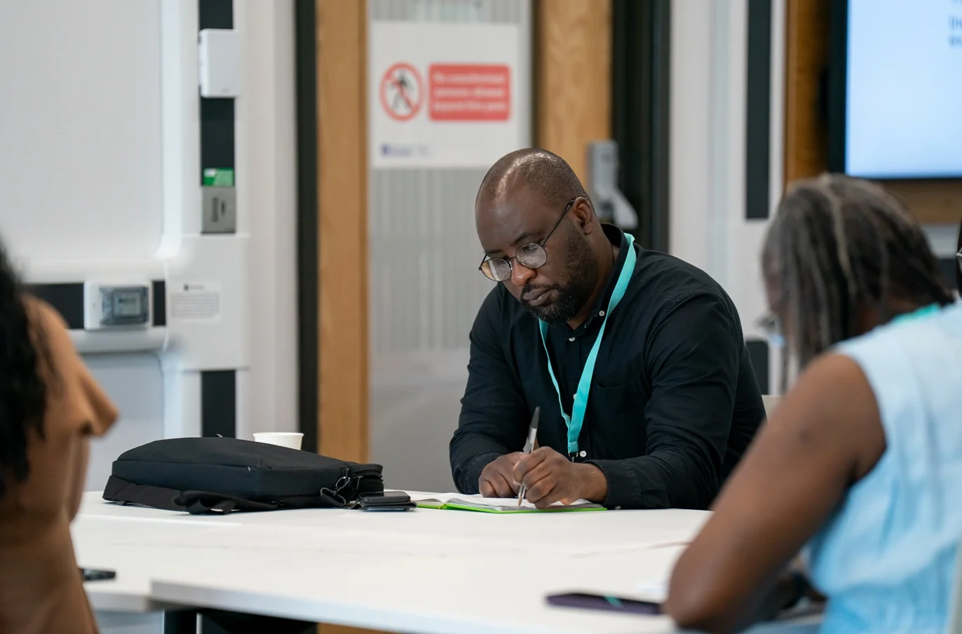 A man sits alone at a table in a classroom marking work in an exercise book