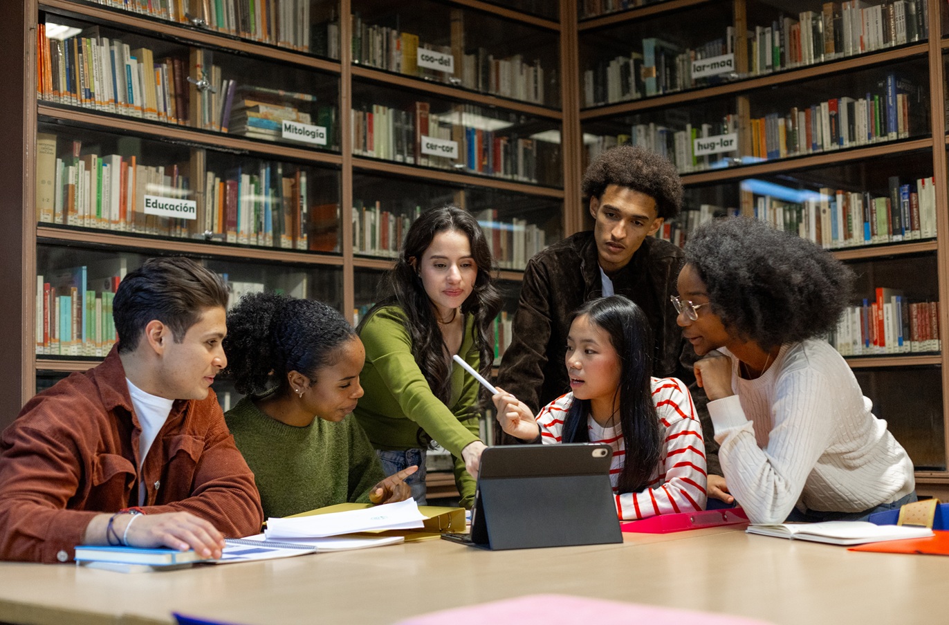 Group of diverse students in a library collaborating around a laptop